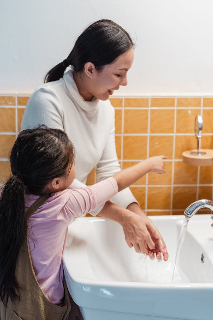 A joyful moment of a mother and daughter washing hands at a bathroom sink, promoting hygiene.