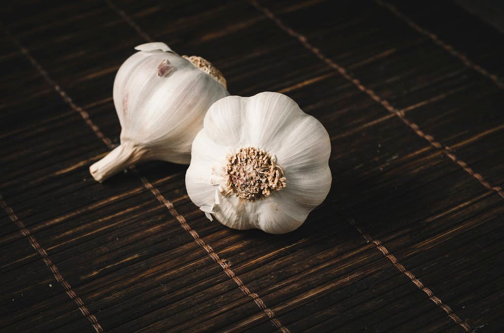 Two fresh garlic bulbs on a dark wooden mat, highlighting aromatic culinary ingredients.